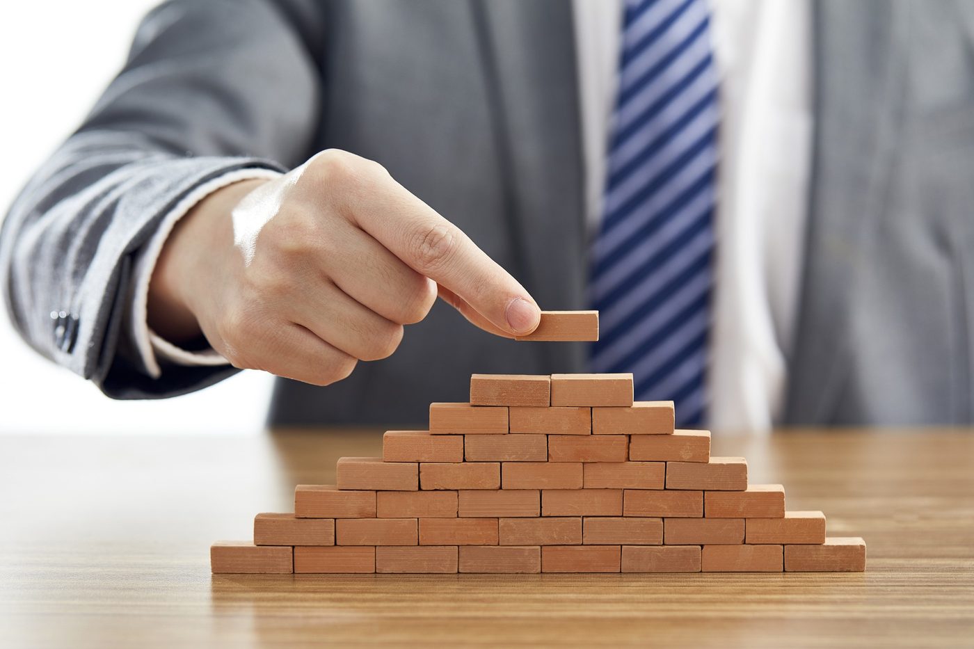 A hand placing the top brick on a small pyramid of bricks